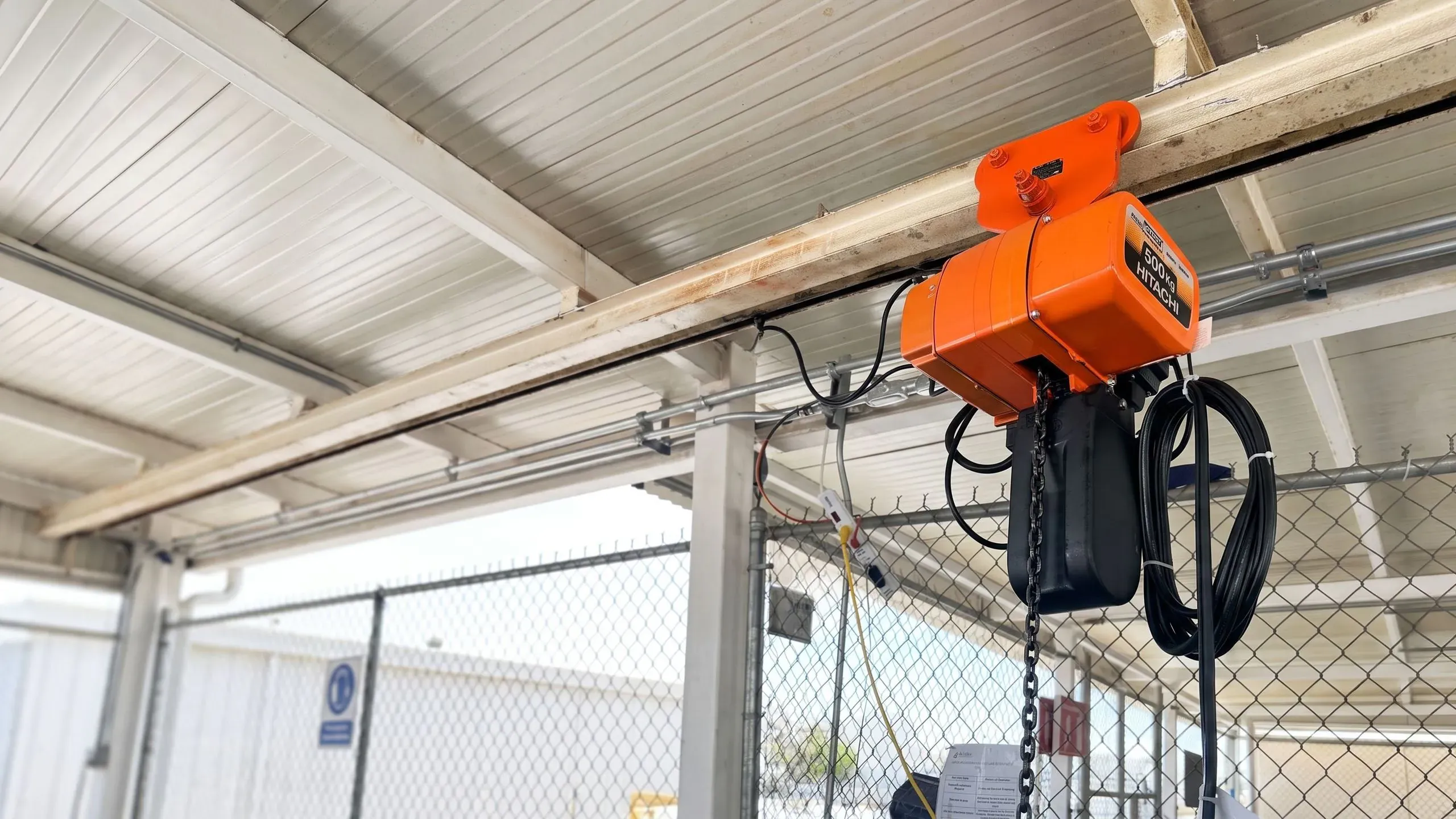 Polipasto eléctrico de cadena Hitachi color naranja instalado en una viga de nave industrial.